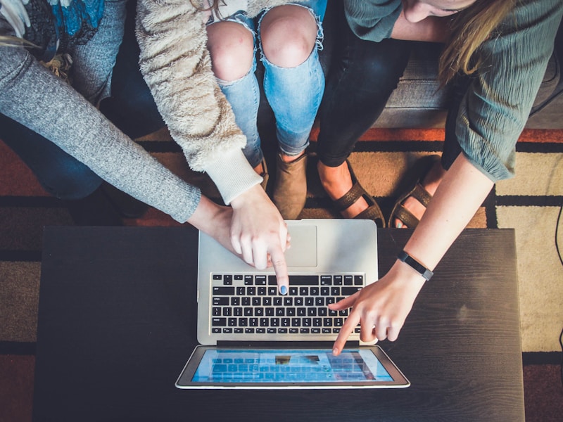 Top view of three people collaborating around a laptop on a wooden coffee table
